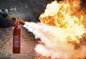 *** Inspector please note - all branding and proprietary information has been removed from the fire extinguisher, just weight/capacity and generic safety information left.  Thanks  *** 

A man using a Carbon Dioxide fire extinguisher to fight a fire.